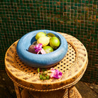 Blue marbled resin decorative bowl filled with limes and passion fruit on rattan side table against tiled wall