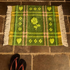 Green tufted bath mat with heart and floral motifs laid on stone floor tiles, viewed from above