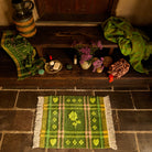 Green plaid tufted bath mat with heart and flower motifs and cream fringe, laid on stone floor from above