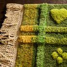 Close-up of green tufted bath mat showing cream twisted fringe, yellow plaid border, and raised heart motif texture