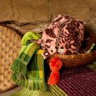 Green plaid fringed hand towel styled with a pink floral toiletry bag and wicker basket in a rustic setting