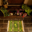Overhead view of a green plaid hand towel with heart and flower motifs laid flat on a stone floor in a rustic bathroom