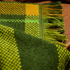 Close-up corner detail of a green and yellow plaid hand towel showing woven texture and multicolour fringe trim