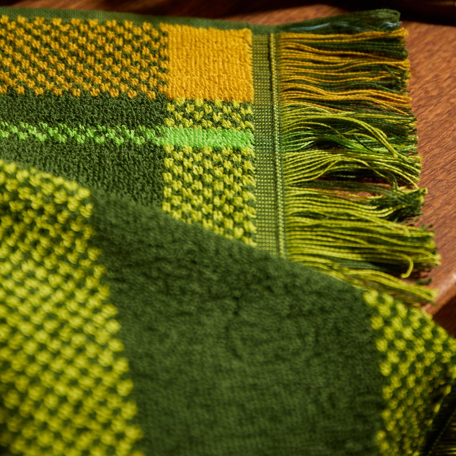 Close-up corner detail of a green and yellow plaid hand towel showing woven texture and multicolour fringe trim