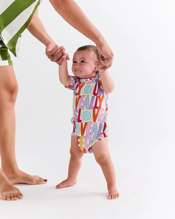 Toddler standing up wearing the Kip & Co x The Beatles All You Need Is Love Organic Short Sleeve Romper