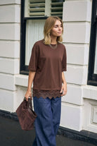Side profile of model wearing chocolate brown Lacey Tee with decorative lace edging