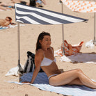 Lady sitting under Swim Shady solo beach shade with navy and white stripes