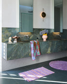 Kip & Co Lavender Field Stripe Bath Mat styled on modern bathroom floor with marble vanity and matching towel