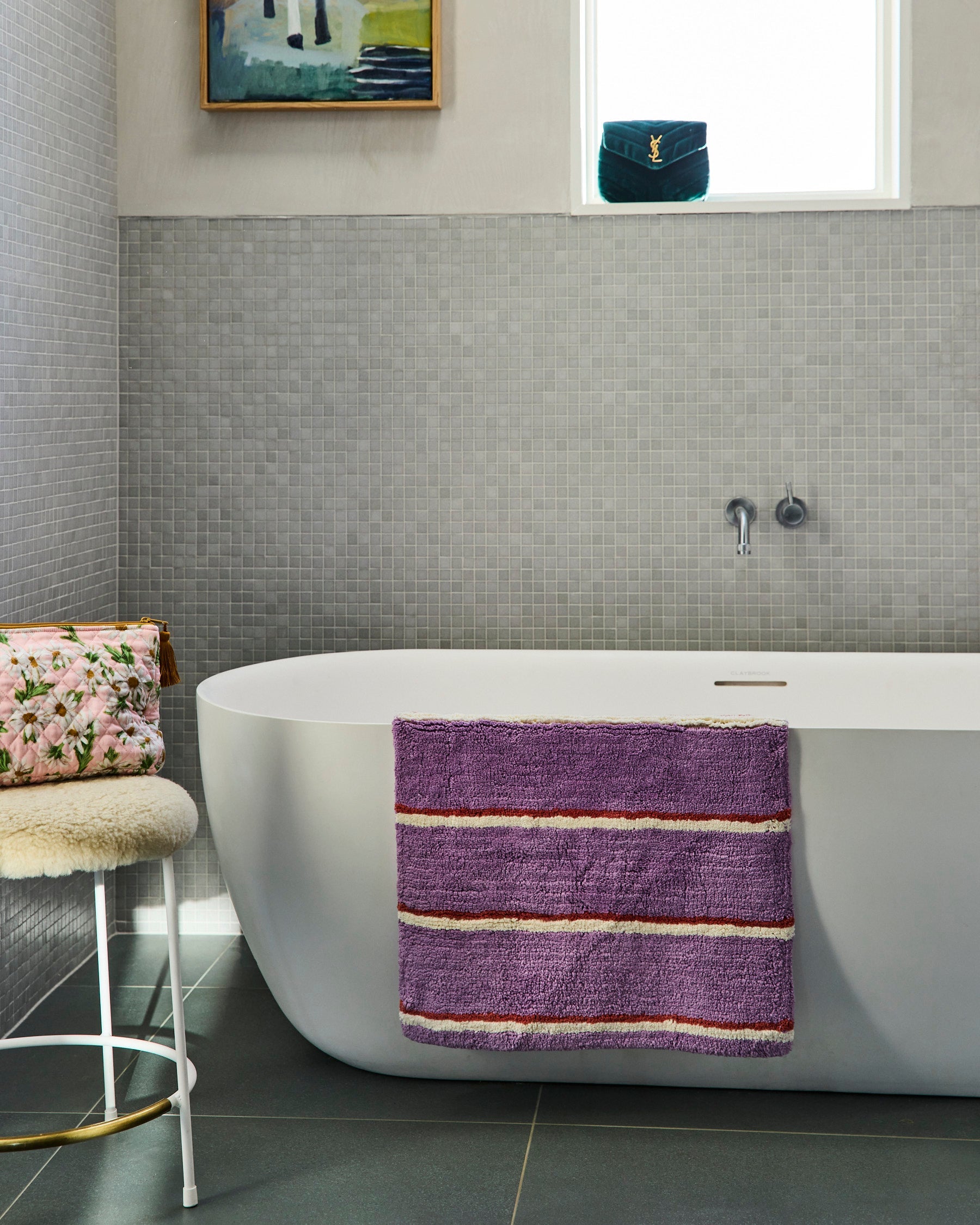 Purple striped bath mat by Kip & Co draped over white freestanding bathtub in contemporary bathroom setting
