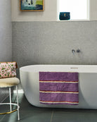 Purple striped bath mat by Kip & Co draped over white freestanding bathtub in contemporary bathroom setting