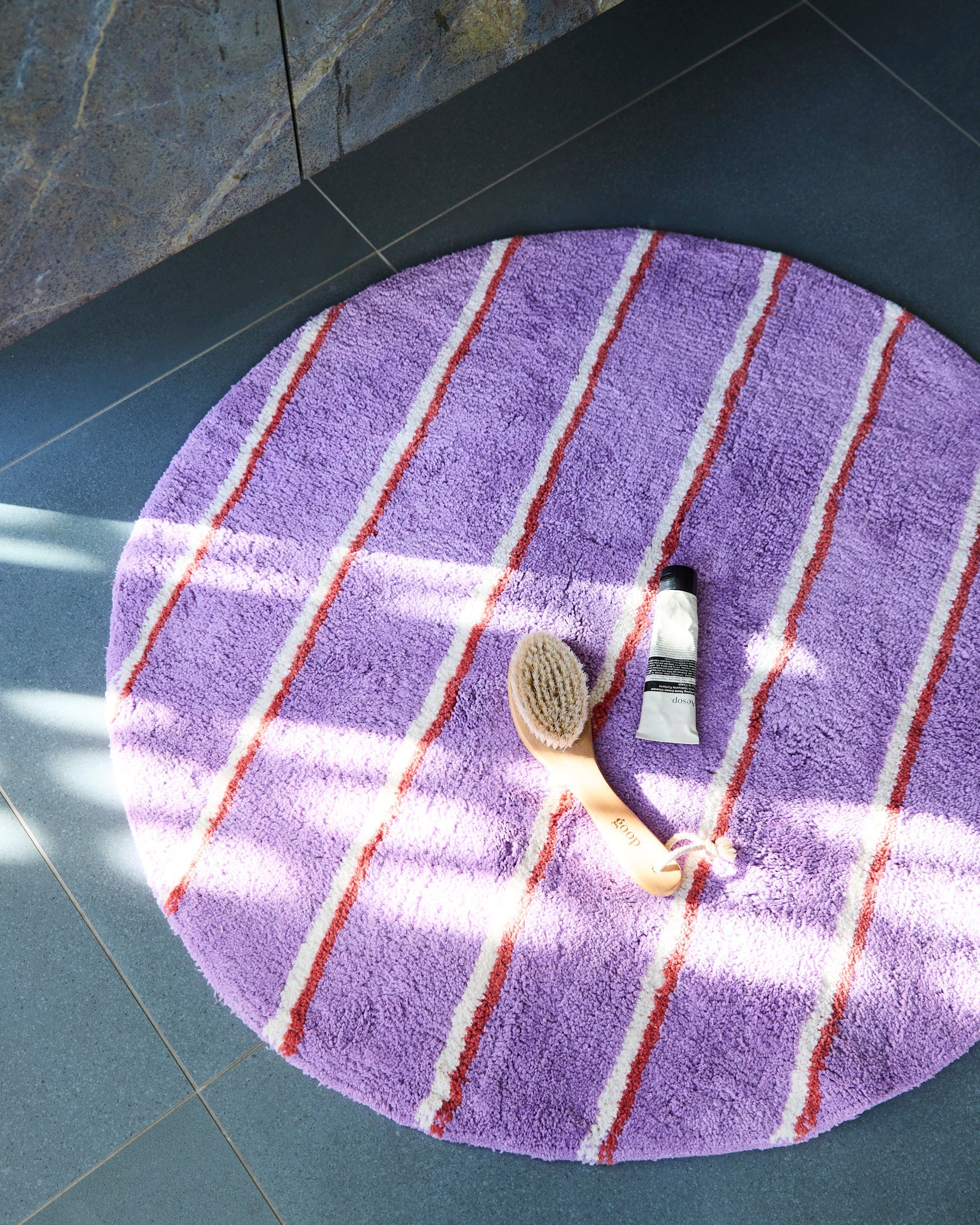 Overhead view of Kip & Co Lavender Field Stripe Round Bath Mat with red white striped pattern and bath accessories