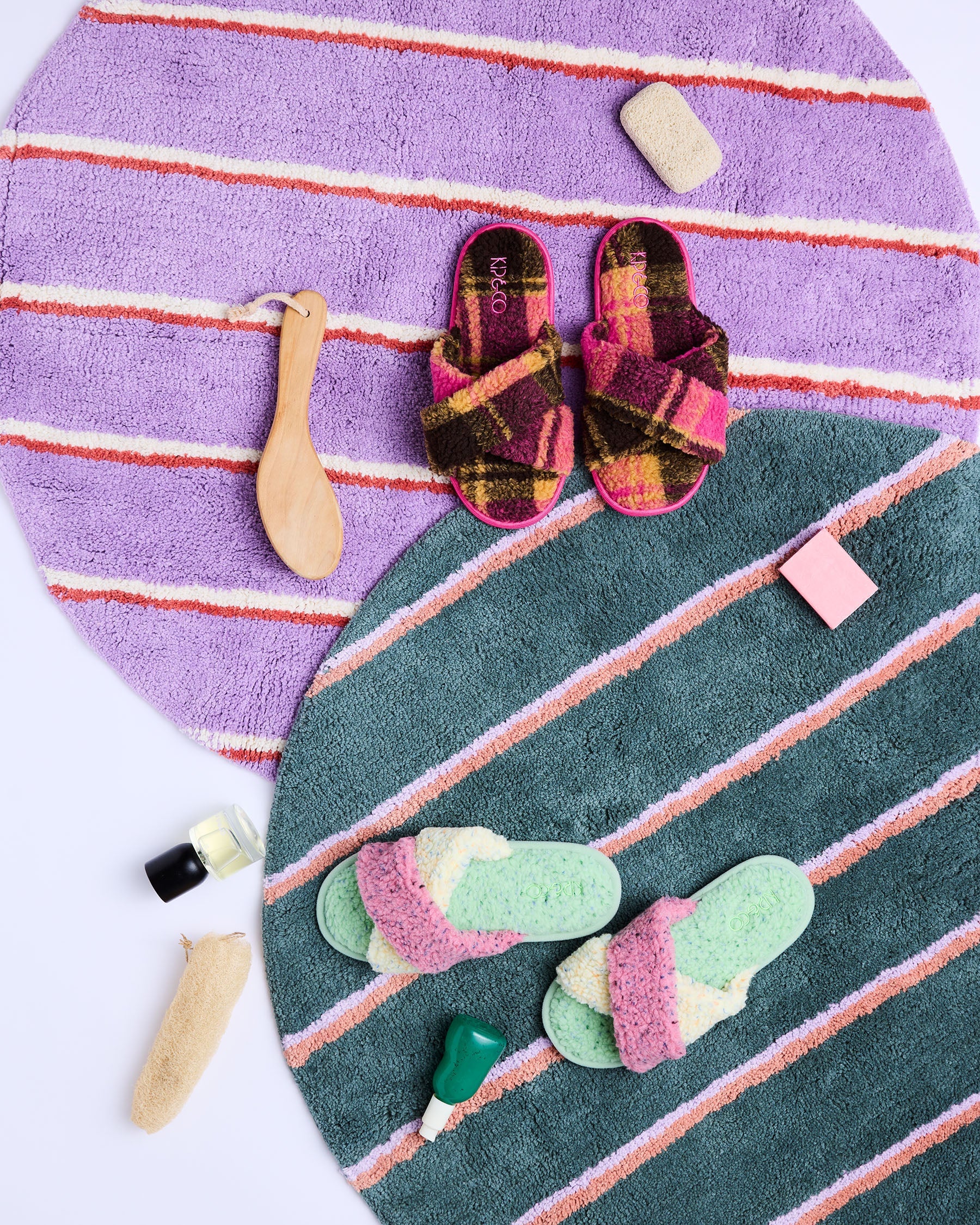Flat lay styling of striped round bath mat showing lavender and teal sections with colorful slippers and bath tools