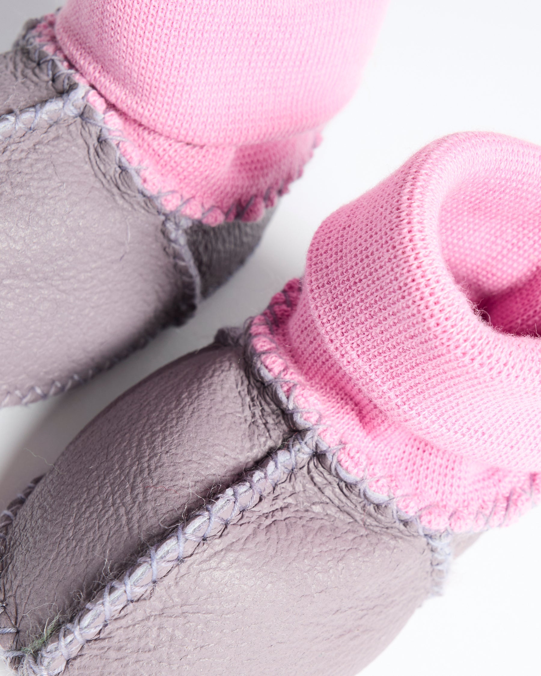 Detail view of lilac baby bootie showing pink knit texture and gray leather sole stitching