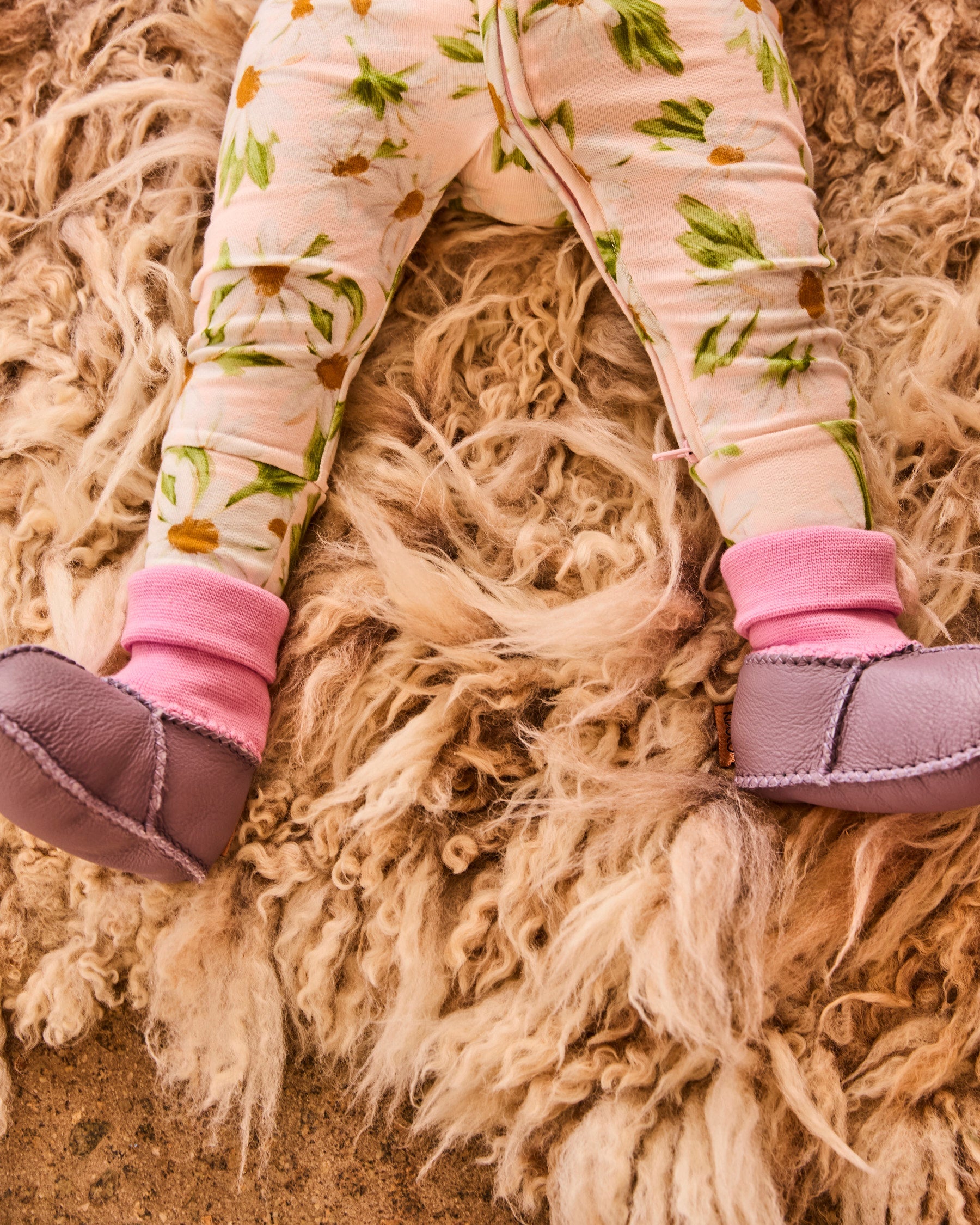 Flat lay of baby legs in lilac booties with pink cuffs on textured fur surface