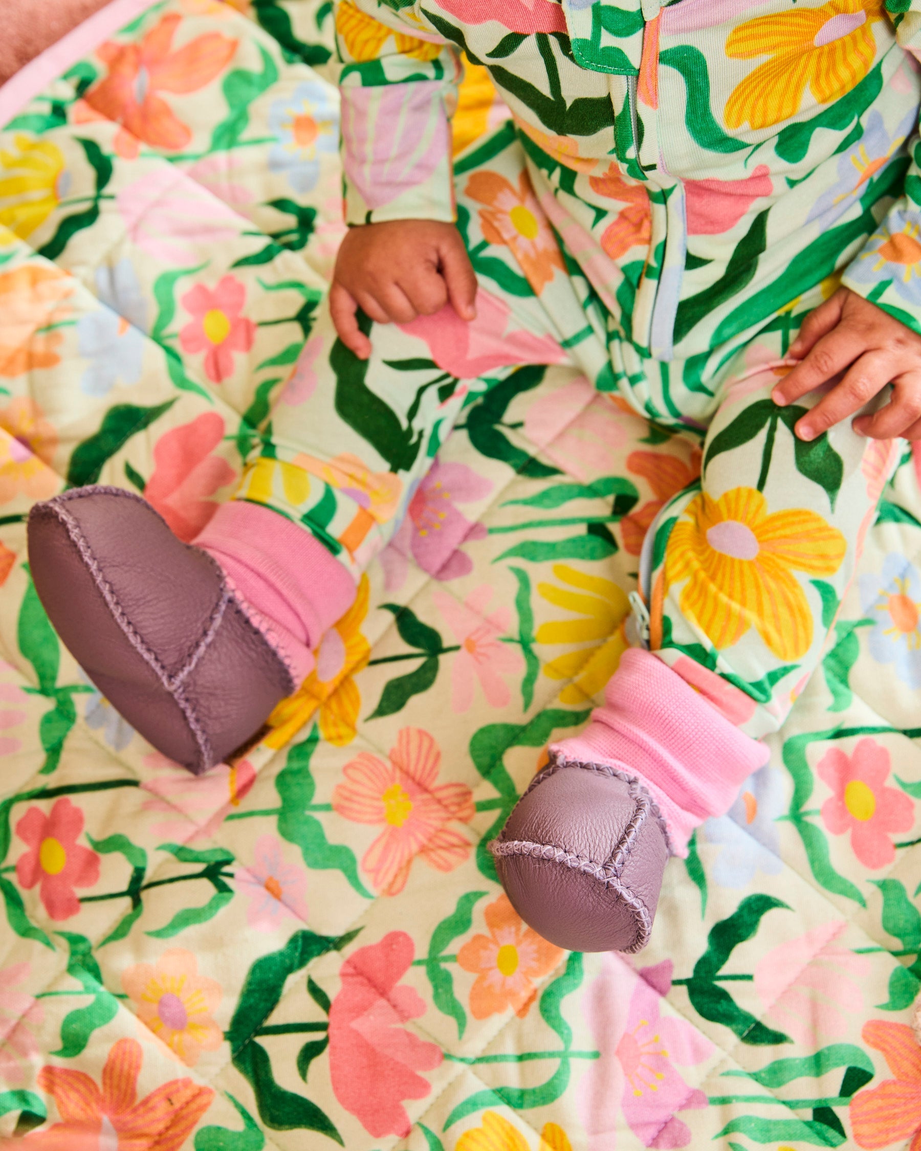 Baby hands and feet wearing lilac booties with pink knit cuffs on floral outfit