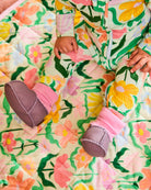 Baby hands and feet wearing lilac booties with pink knit cuffs on floral outfit