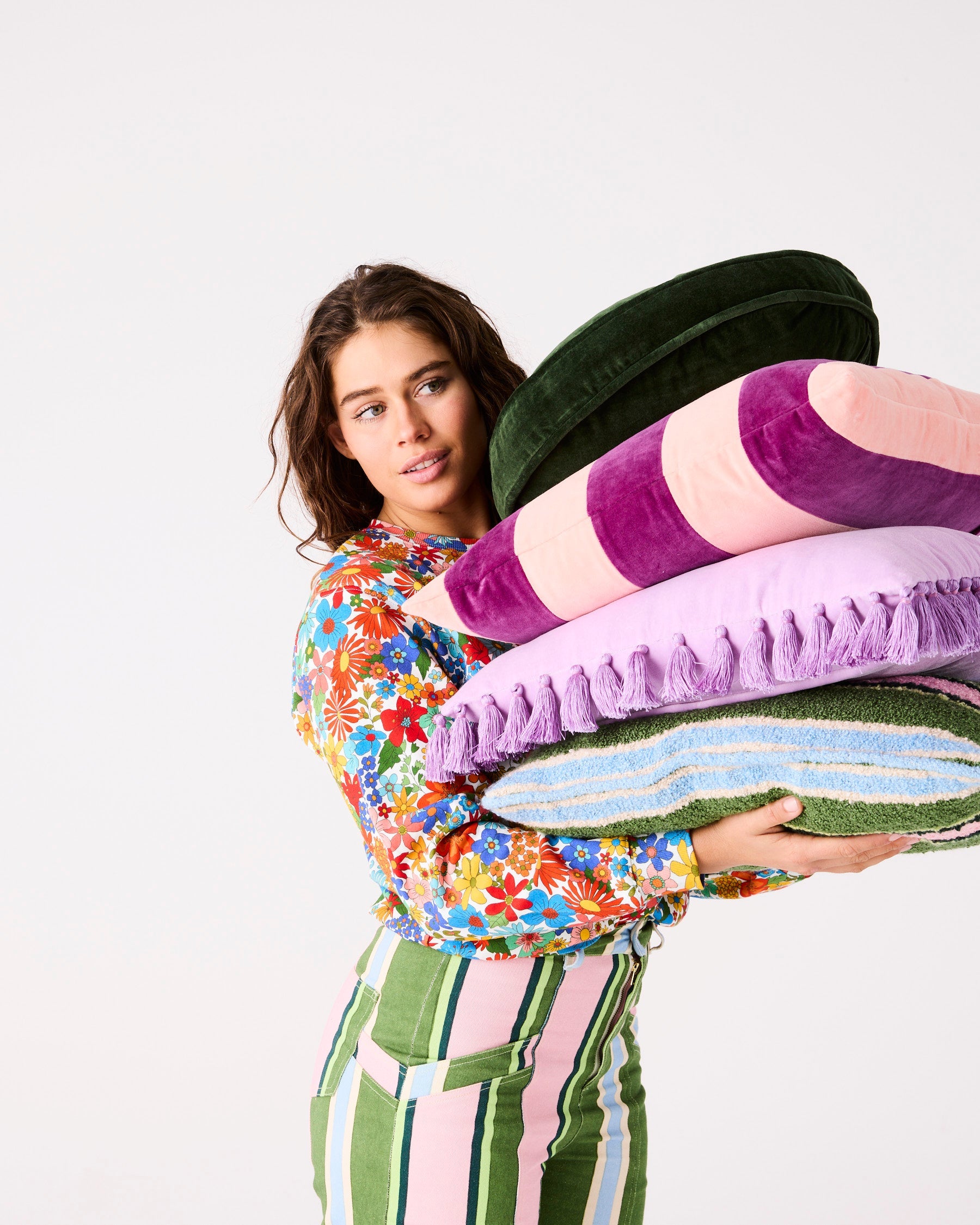 Woman holding stack of colorful velvet cushions including lilac purple tassel cushion