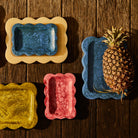 Crimson pink marbled resin scalloped tray shown in a group flat-lay with other coloured trays on wood