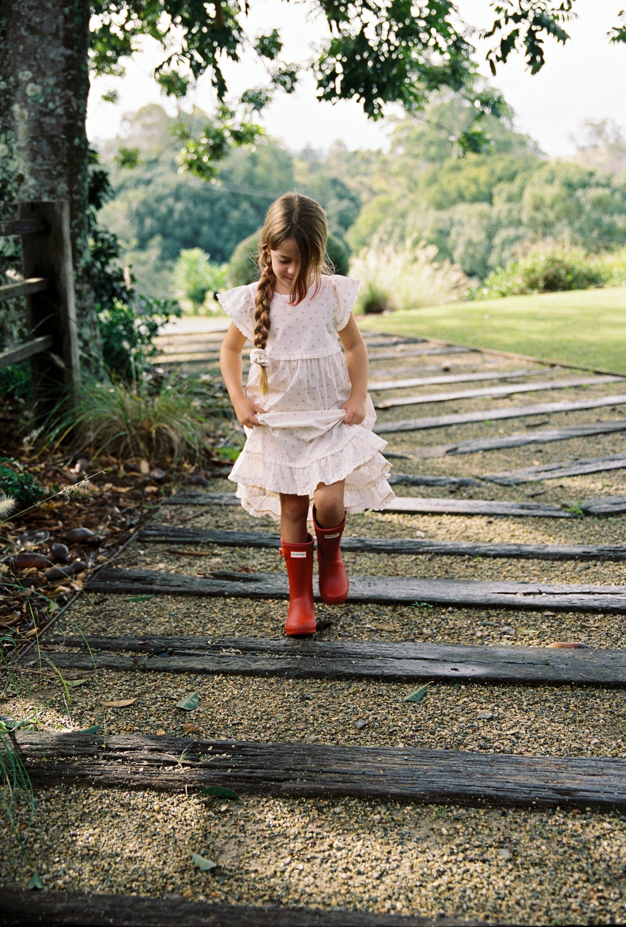 Child wearing white Lola Dress with rose pattern walking on wooden pathway outdoors