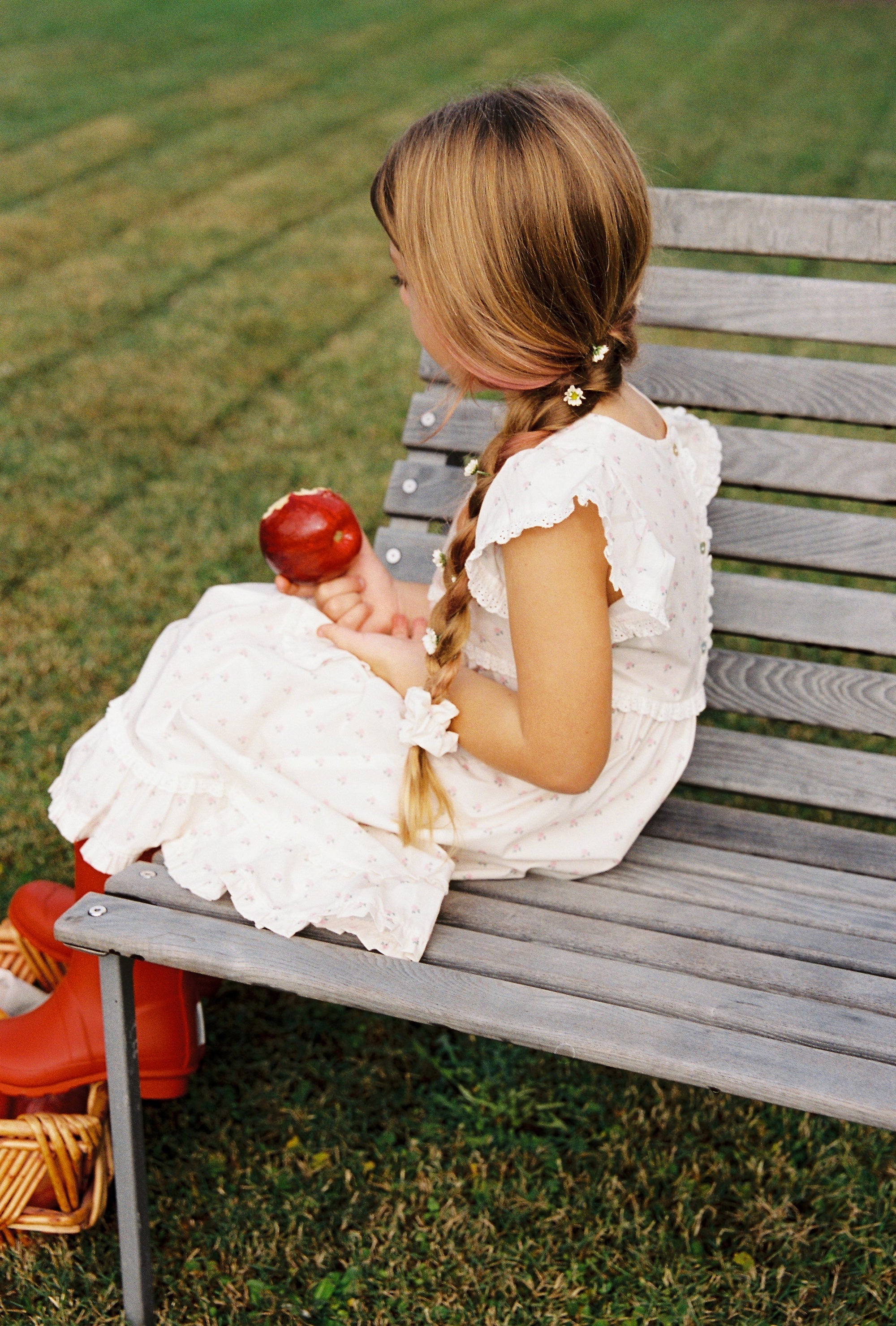 Side view of child in Lola Dress with roses print sitting on wooden bench