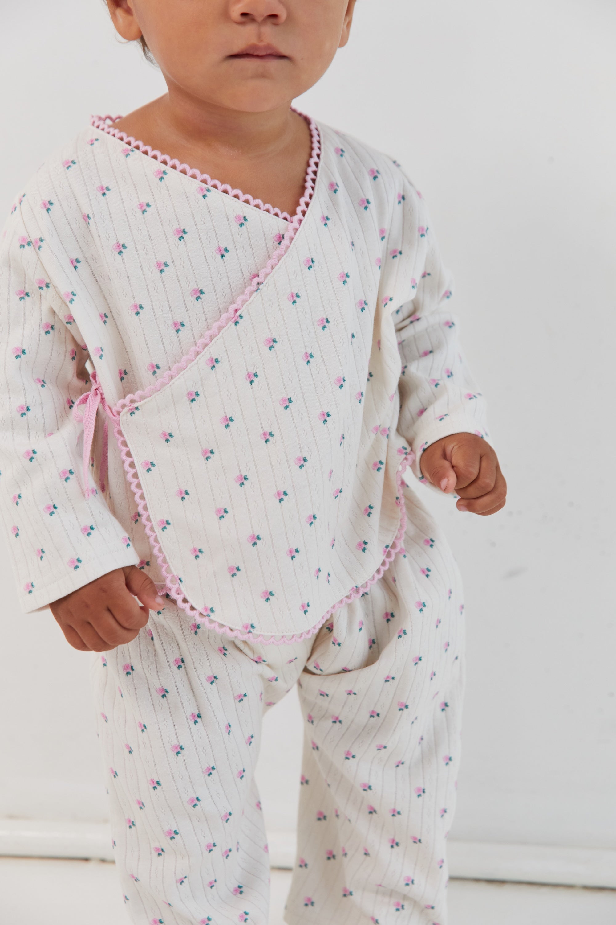 Close-up front view of child in Lolly Set wrap top with roses print and pink binding