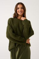 Close-up front view of an olive green oversized ribbed knit sweater with wide sleeves on a smiling woman
