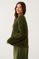 Side view of an olive green oversized chunky ribbed knit sweater showing volume and long wide sleeves
