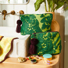 Green patterned pouch with burgundy tassels on a wooden surface next to a plant and sink.