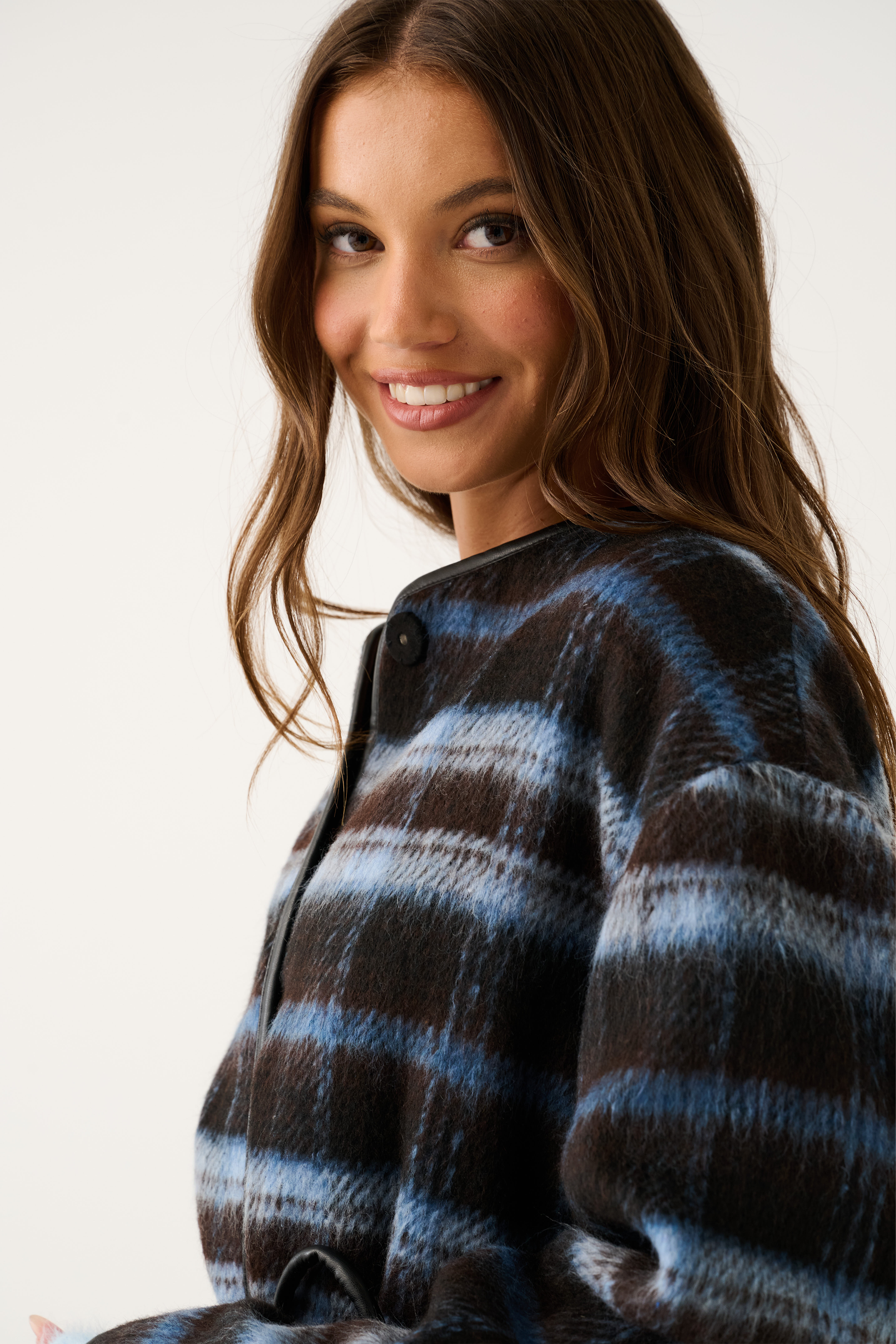 Close-up side view of a blue and brown check jacket showing the black leather trim neckline and snap button