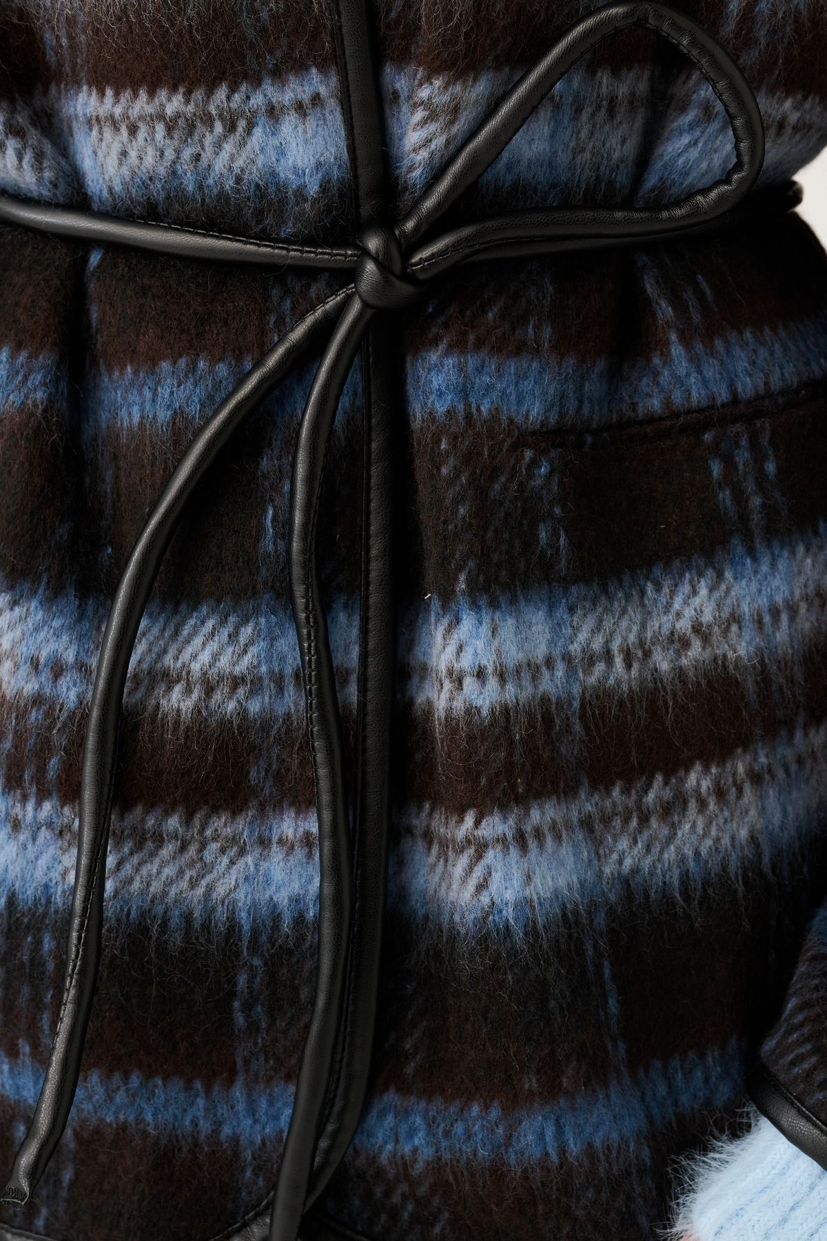 Detail shot of the black leather knot tie belt on a blue and brown check textured jacket
