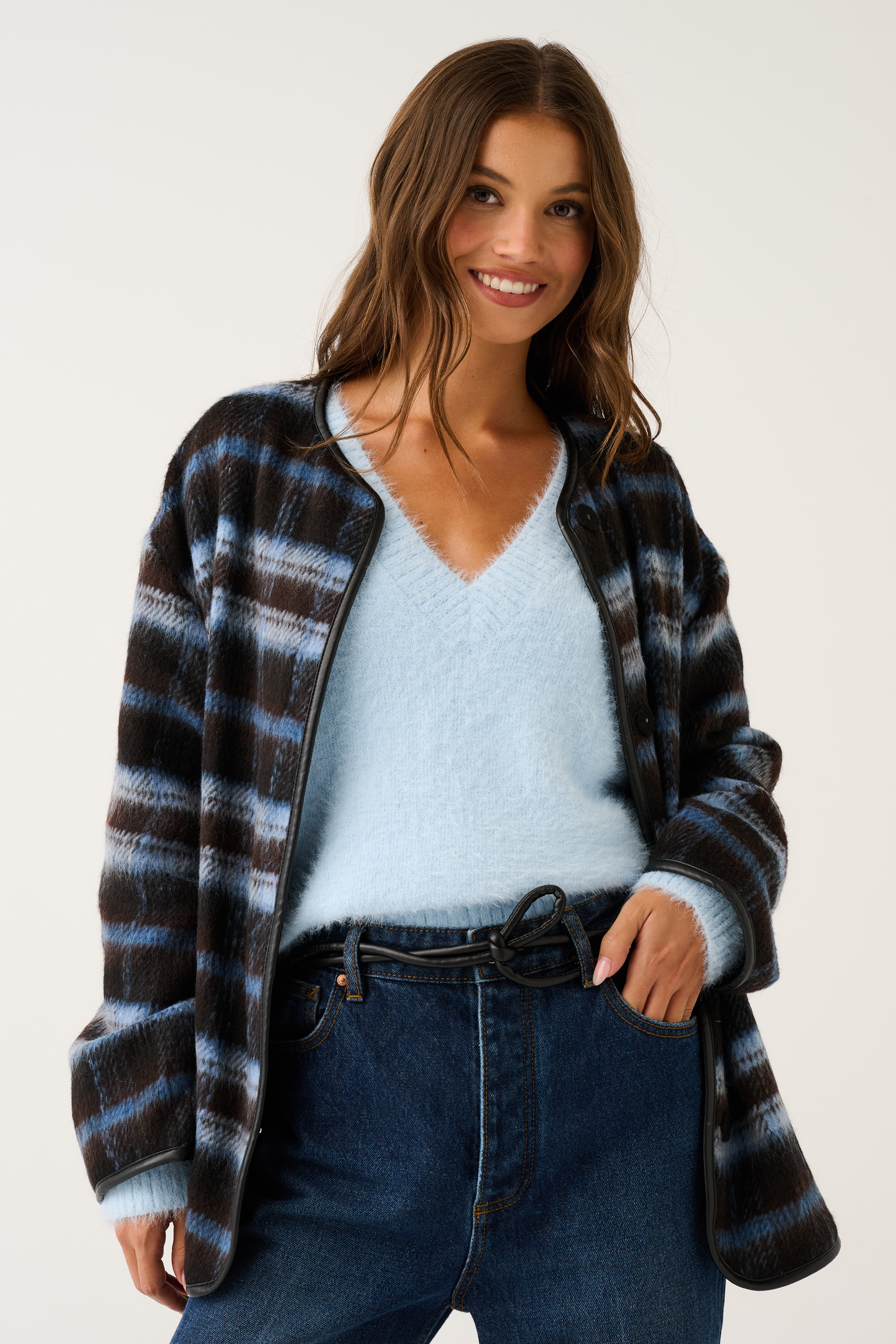 Open-front blue and brown check jacket with black leather trim worn over a pale blue knit sweater and jeans