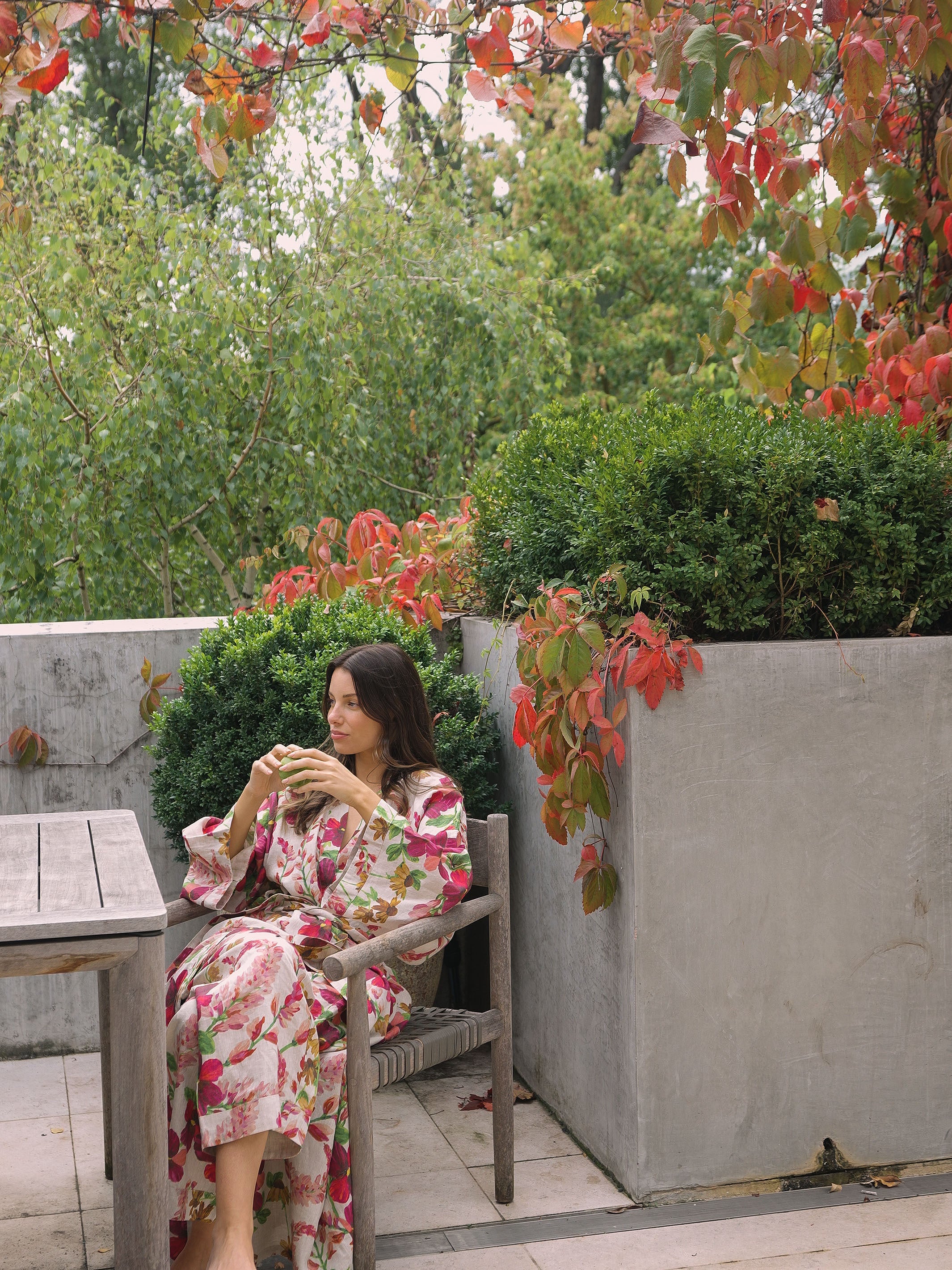 Side view of woman in Lupin Multi Linen Robe with botanical print sitting outdoors on wooden chair