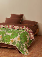 Angled view of Lupin Multi Marigold Leaf quilted throw displaying both green botanical and floral sides