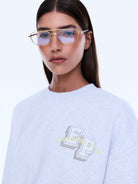 Close-up view of white oversized sweater showing embroidered chest logo detail