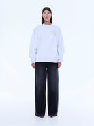 Front view of white oversized sweater showing relaxed fit and embroidered chest detail