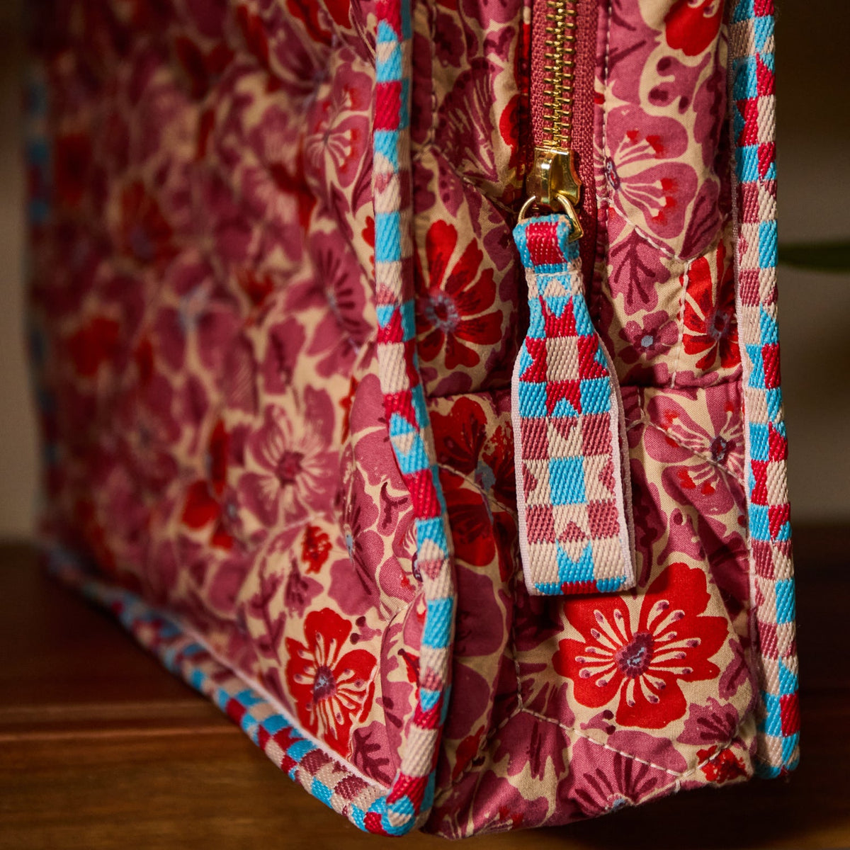Side detail of Poppy Magnolia Vanity Bag highlighting gold zipper, checkered zip pull, and quilted floral sides