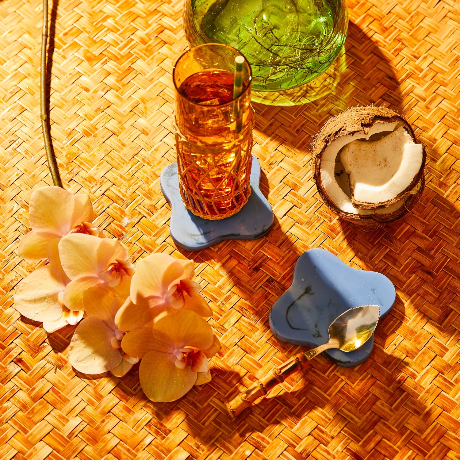 Overhead view of blue marble coasters with cocktail glass and tropical decor on woven mat