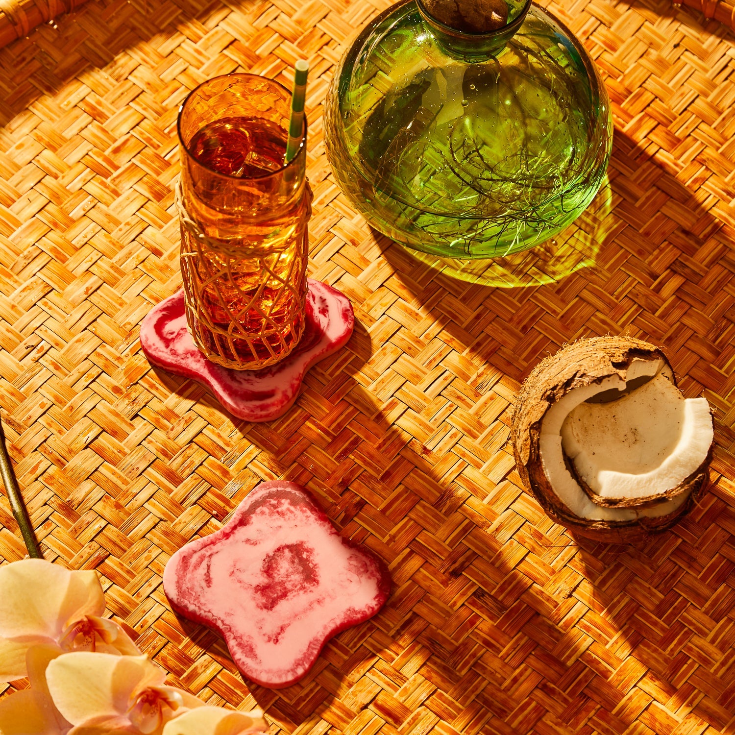 Crimson marbled resin coasters on a woven rattan tray, one holding a cocktail glass, tropical styling
