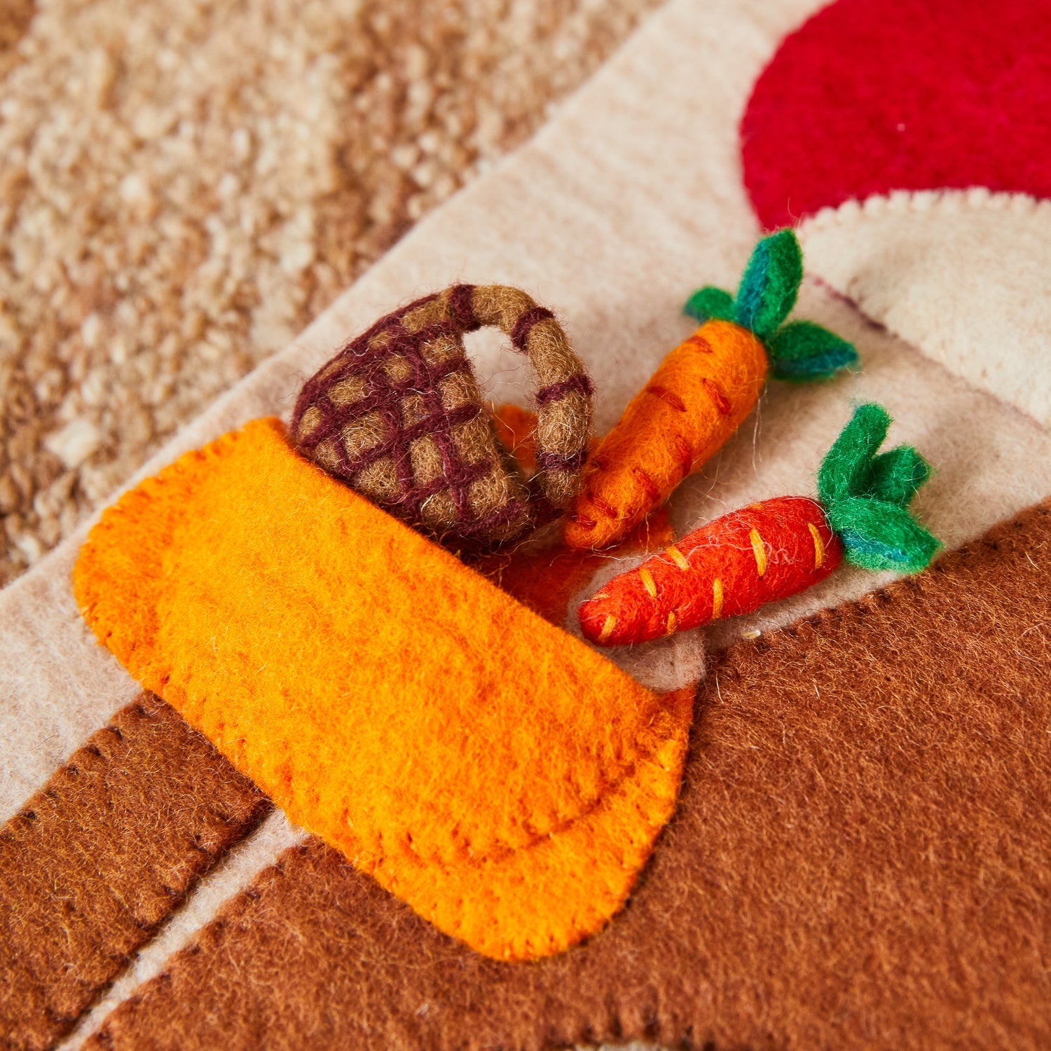 Detail view of yellow felt sun flower with orange center and striped pink mushroom on red cap