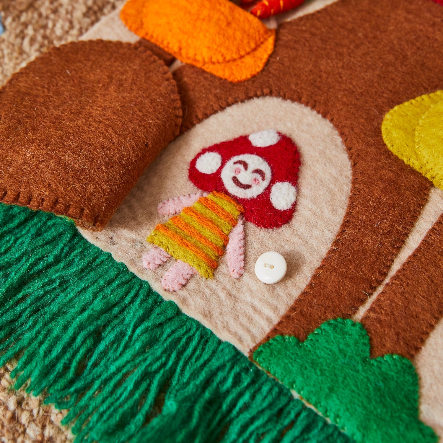 Brown felt mushroom door with white button closure and orange basket detail showing blanket stitching
