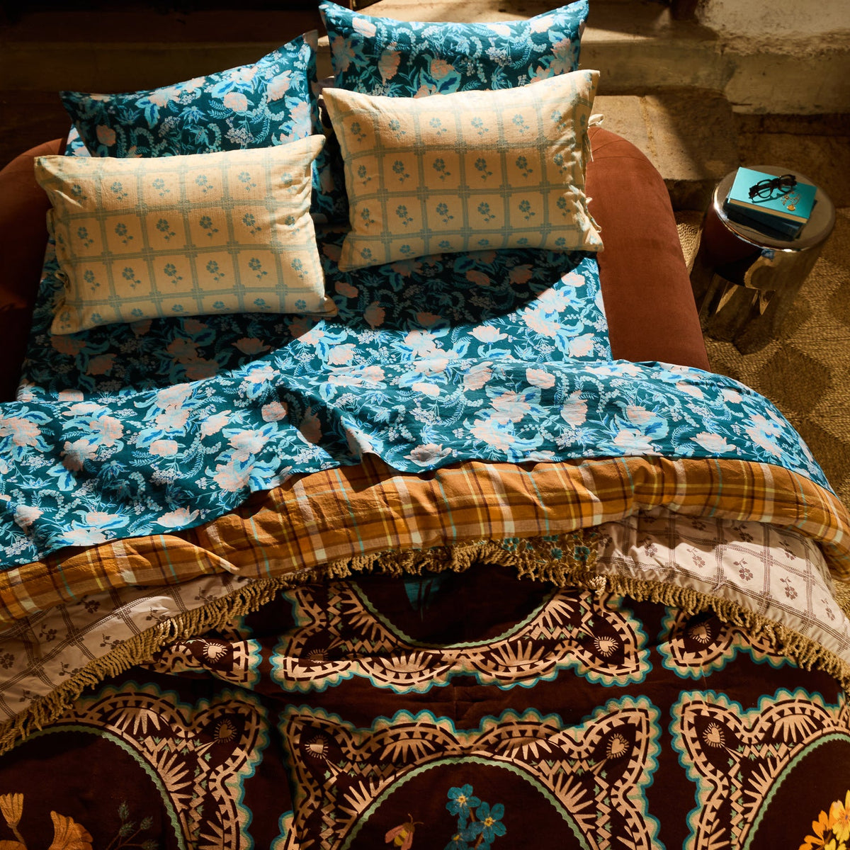 Overhead view of brown velvet bedcover with botanical medallion print and fringe trim layered on a styled boho bed