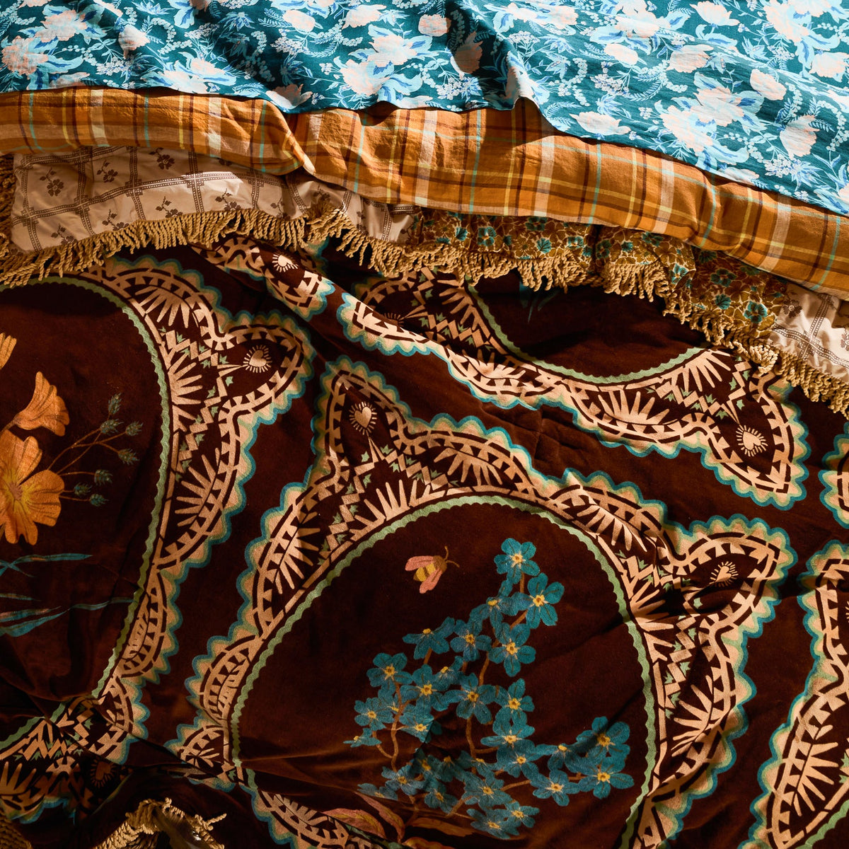 Close-up of brown velvet bedcover surface showing teal floral motifs within ornate medallion frames and gold fringe trim