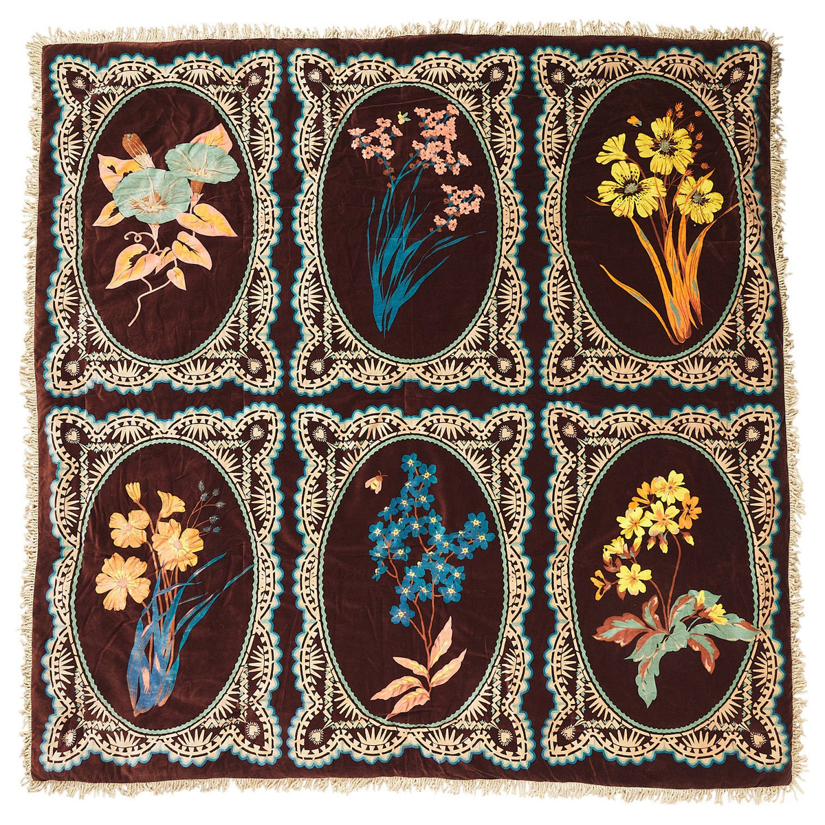 Flat-lay of brown velvet bedcover showing six oval botanical floral medallions in teal, yellow, and pink with cream fringe trim
