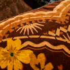 Close-up of brown velvet cushion fabric showing yellow flowers and detailed tribal border pattern with sun motifs