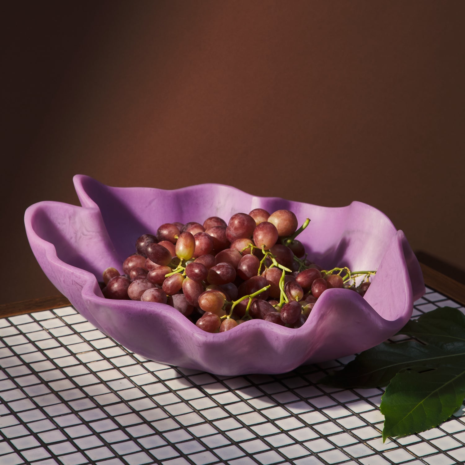 Orchid ceramic bowl filled with red grapes on neutral beige background showing organic shape