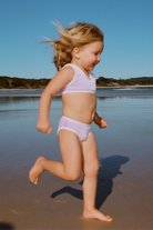 Young child running on the beach wearing a lilac mini stripe bikini bottom with white trim