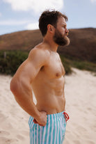 Man wearing blue and white striped swim trunks on a sandy beach.