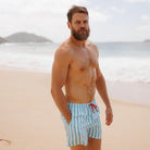 Man wearing blue and white striped swim shorts with a red bow on a beach.