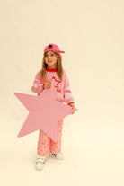 Full body shot of child in pink Neve Knit sweater with red star design and pink baseball cap
