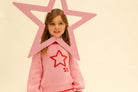 Child wearing pink Neve Knit sweater standing behind large pink star outline prop